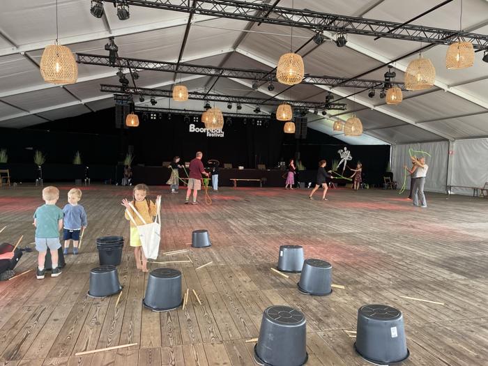 Kinderen trommelen op emmers en volwassenen doen rope flow in een festivaltent