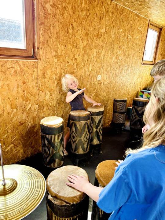 Kinderen trommelen op djembés in een houten ruimte
