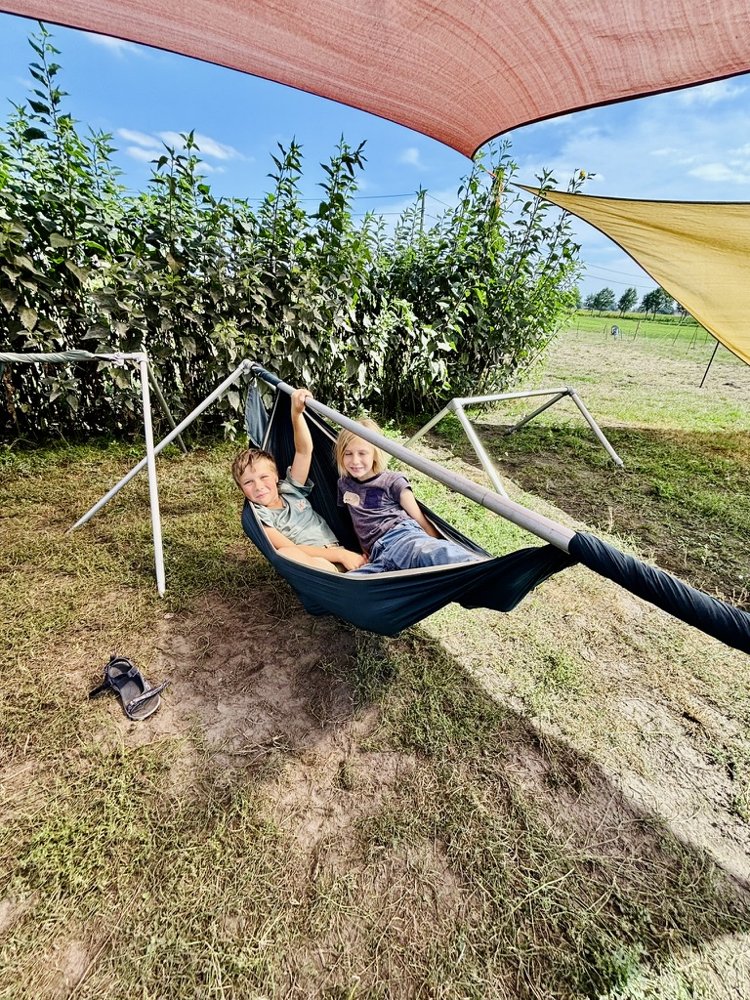 Twee kinderen chillen samen in de hangmat onder een zonnezeil