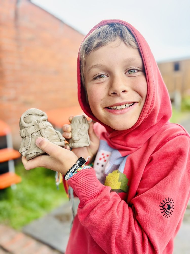 Een lachende jongen toont zijn zelfgemaakte kleifiguren