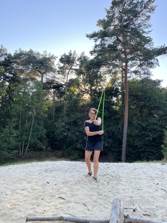 Mieke doet lachend rope flow met een groen touw in het zand, tussen de dennen